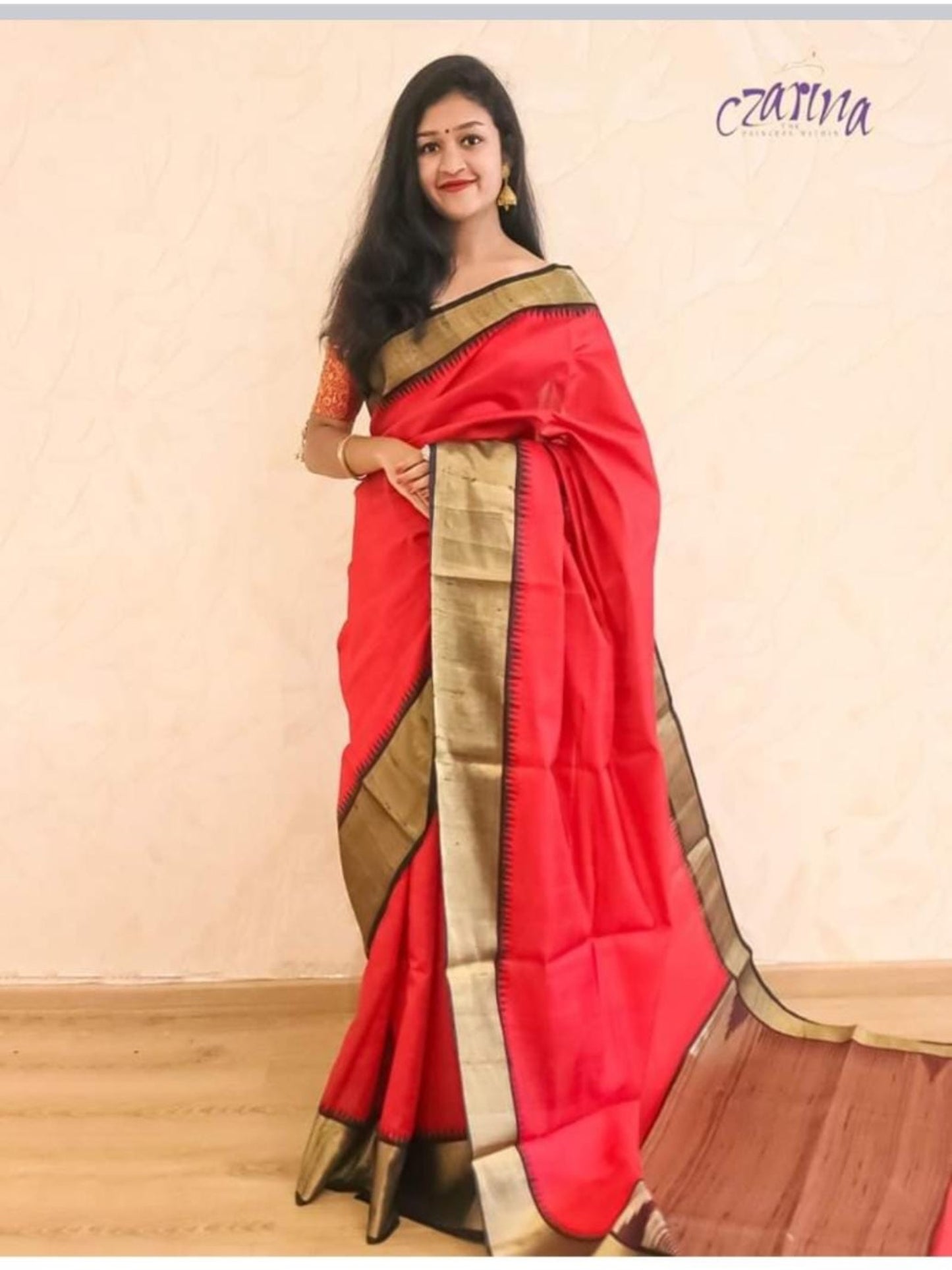 A RAVISHING RAW SILK SAREE IN RED,EMBELLISHED WITH STRIKING BLACK AND GOLD BORDERS AND PALLU